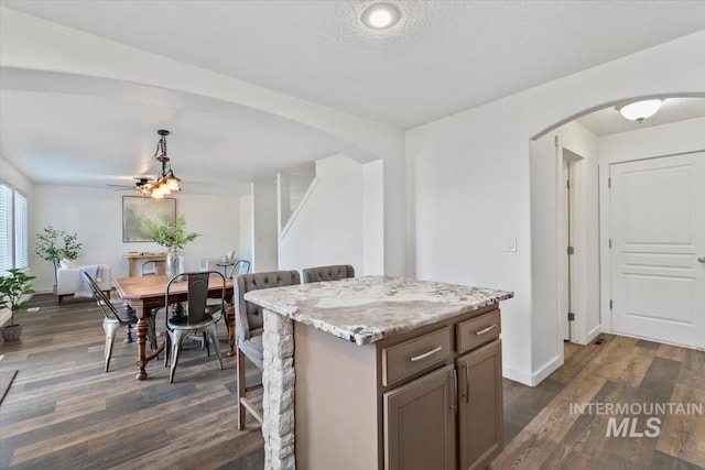 kitchen featuring a textured ceiling, ceiling fan, dark hardwood / wood-style floors, a kitchen island, and a breakfast bar