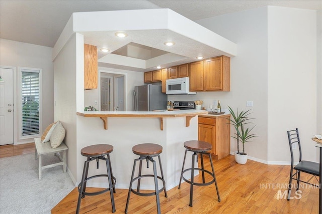 14325 W Comisky, Boise, ID 83713 - kitchen with freestanding refrigerator, white microwave, a kitchen breakfast bar, light wood-type flooring, and brown cabinets