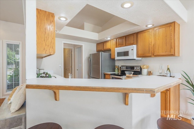 14325 W Comisky, Boise, ID 83713 - kitchen featuring appliances with stainless steel finishes, a breakfast bar, a peninsula, light countertops, and brown cabinetry