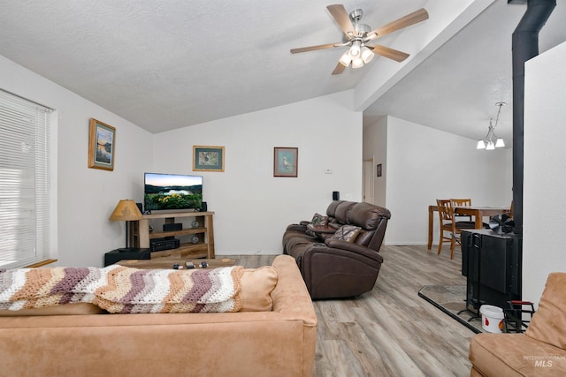 living room featuring light hardwood / wood-style floors, a wood stove, a textured ceiling, lofted ceiling, and ceiling fan with notable chandelier