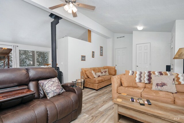 living room with lofted ceiling, ceiling fan, light hardwood / wood-style floors, and a wood stove