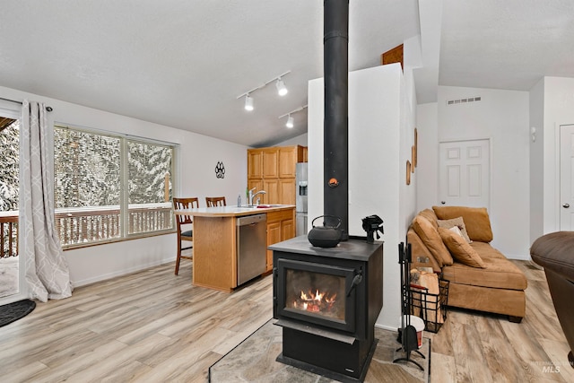 living room with sink, light hardwood / wood-style flooring, vaulted ceiling, and a wood stove