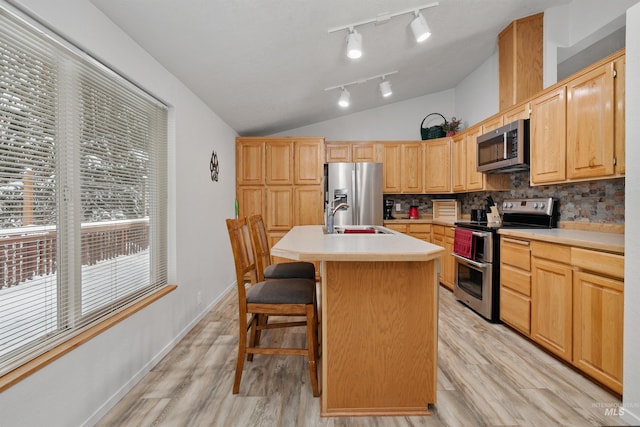 kitchen with stainless steel appliances, a kitchen bar, light brown cabinetry, backsplash, and a kitchen island with sink