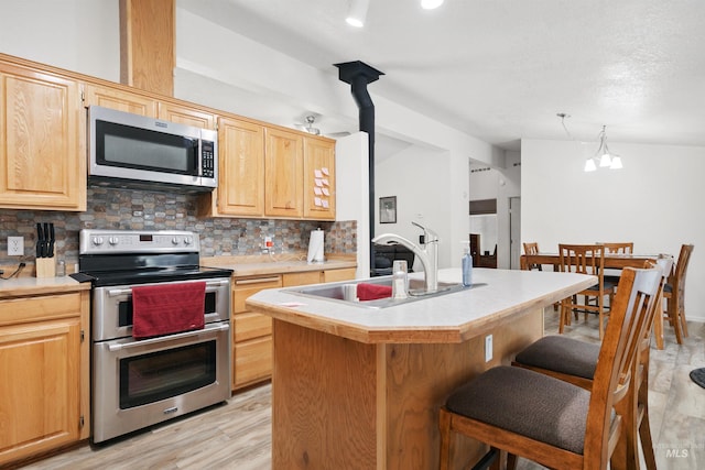 kitchen featuring a center island with sink, a chandelier, backsplash, and appliances with stainless steel finishes