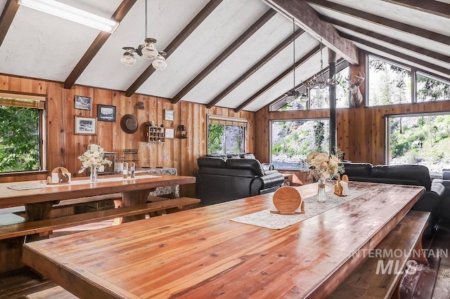 dining space featuring beamed ceiling, a healthy amount of sunlight, high vaulted ceiling, and wooden walls