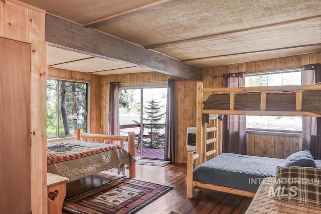 bedroom with beam ceiling, dark wood-type flooring, wood walls, and access to exterior