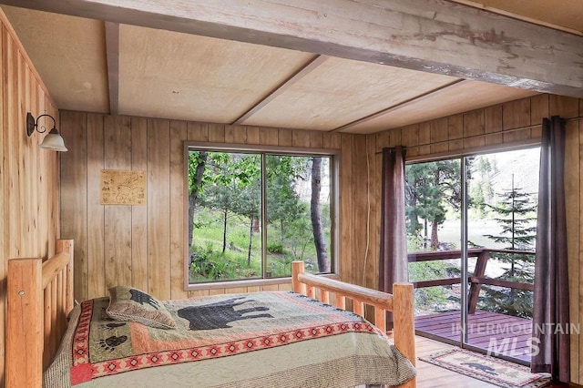 bedroom featuring beamed ceiling, wooden walls, access to outside, and multiple windows