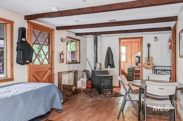 bedroom with beam ceiling, hardwood / wood-style flooring, and a wood stove