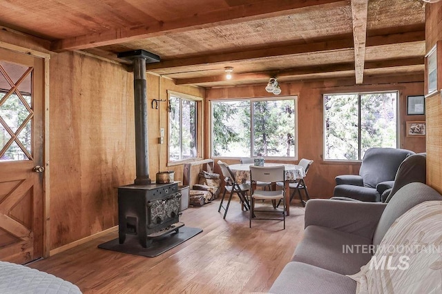 living room featuring beam ceiling, wood walls, wood-type flooring, and a wood stove