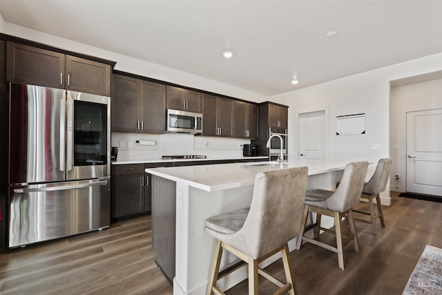 kitchen with a center island with sink, sink, dark wood-type flooring, appliances with stainless steel finishes, and a breakfast bar area