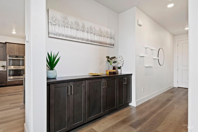 bar featuring double oven, hardwood / wood-style floors, and dark brown cabinetry