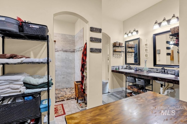 bathroom with double sink, a tile shower, and tile patterned floors