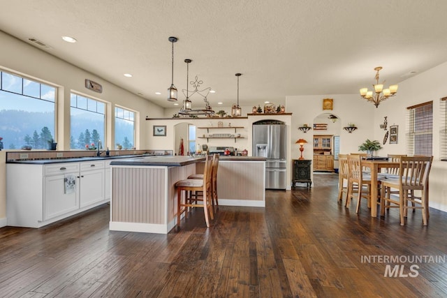 kitchen with stainless steel refrigerator with ice dispenser, decorative light fixtures, a kitchen island, and white cabinets