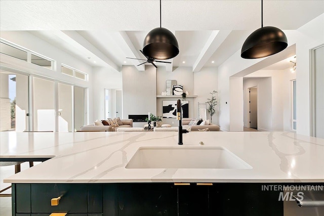 kitchen featuring light stone countertops, a center island with sink, ceiling fan, and decorative light fixtures