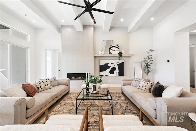 living room with beamed ceiling, wood-type flooring, a large fireplace, and ceiling fan