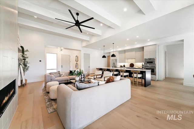 living room with ceiling fan, beamed ceiling, a high ceiling, and light wood-type flooring