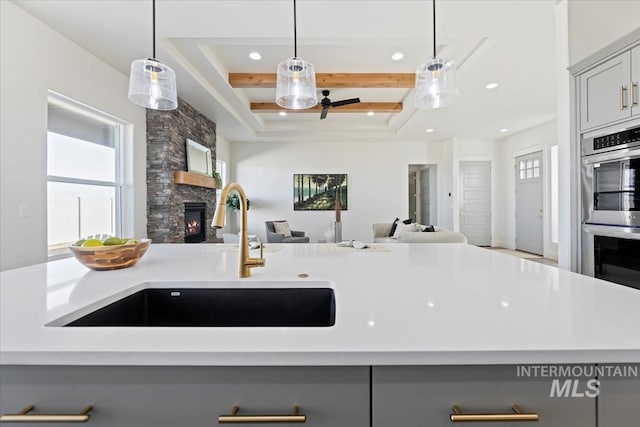 kitchen featuring a raised ceiling, sink, gray cabinetry, a stone fireplace, and double oven