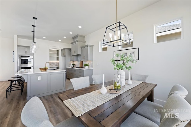 dining space with a healthy amount of sunlight, dark wood-type flooring, sink, and a notable chandelier