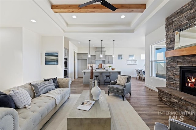 living room featuring ceiling fan, hardwood / wood-style flooring, a stone fireplace, and beamed ceiling