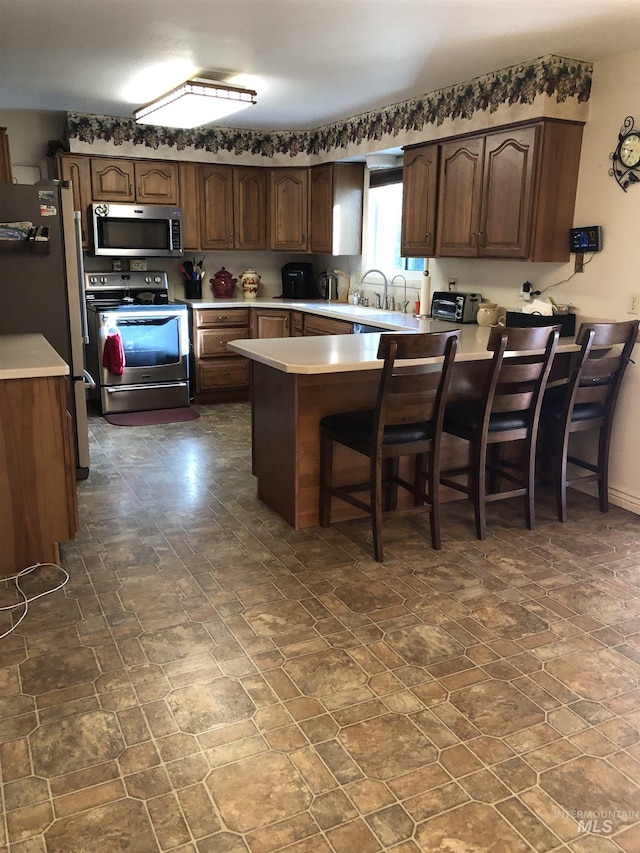 2726 Fairmont Dr, Burley, ID 83318 - kitchen featuring stainless steel appliances, a peninsula, light countertops, a kitchen breakfast bar, and dark stone finish floors