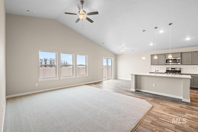 unfurnished living room featuring a textured ceiling, ceiling fan, sink, high vaulted ceiling, and light hardwood / wood-style floors