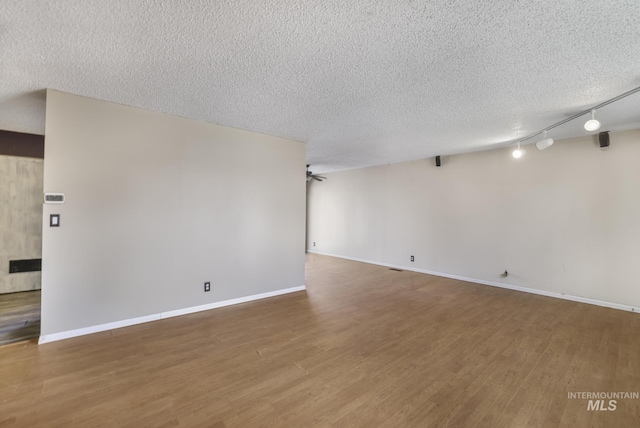 unfurnished room with track lighting, baseboards, wood finished floors, and a textured ceiling