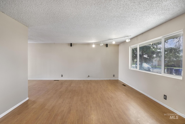 unfurnished room with track lighting, baseboards, a textured ceiling, and wood finished floors