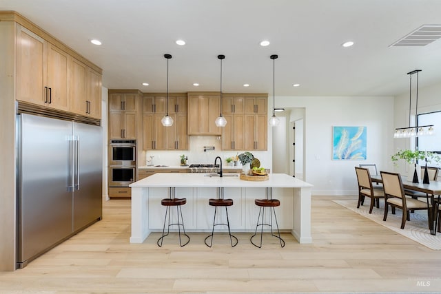 kitchen featuring appliances with stainless steel finishes, light hardwood / wood-style floors, a breakfast bar area, and an island with sink