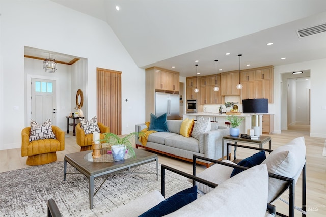 living room with high vaulted ceiling, light wood-type flooring, and an inviting chandelier