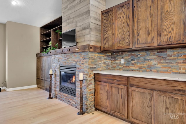 kitchen with a stone fireplace, light hardwood / wood-style flooring, and tasteful backsplash