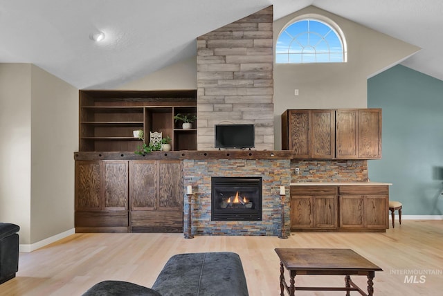 living room featuring a stone fireplace, light hardwood / wood-style flooring, and lofted ceiling