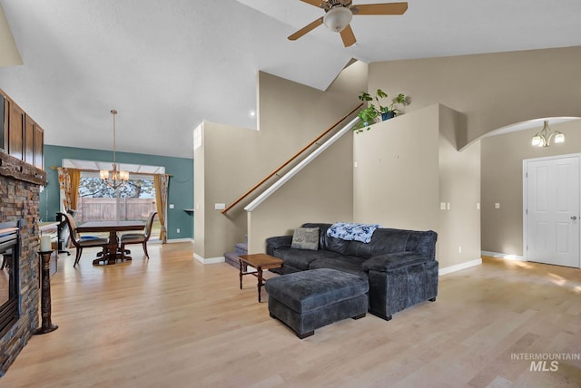 living room featuring a stone fireplace, ceiling fan with notable chandelier, light hardwood / wood-style floors, and lofted ceiling