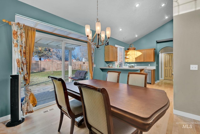 dining room with light wood-type flooring, high vaulted ceiling, and an inviting chandelier