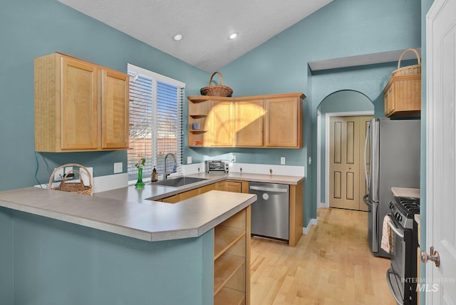 kitchen with sink, kitchen peninsula, vaulted ceiling, appliances with stainless steel finishes, and light wood-type flooring