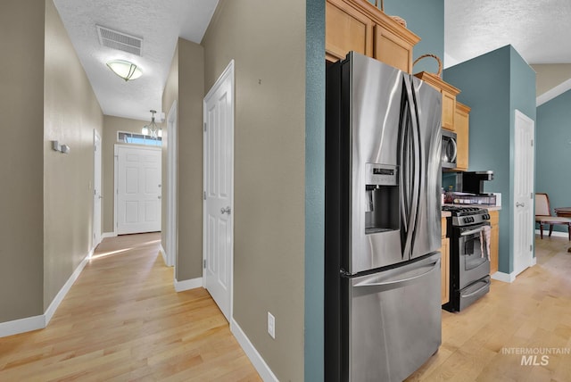 kitchen with appliances with stainless steel finishes, light wood-type flooring, a textured ceiling, and light brown cabinetry