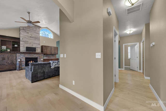 hall featuring lofted ceiling, light hardwood / wood-style flooring, and a textured ceiling