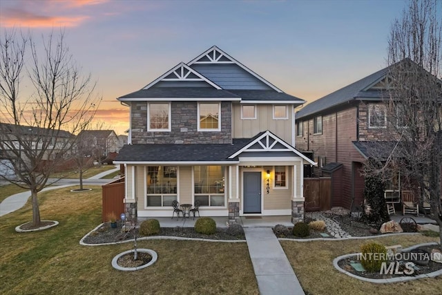 craftsman house with covered porch, board and batten siding, a front yard, fence, and stone siding