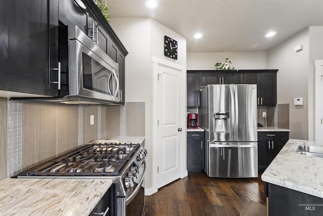 kitchen featuring dark wood-style flooring, stainless steel appliances, tasteful backsplash, a sink, and light stone countertops