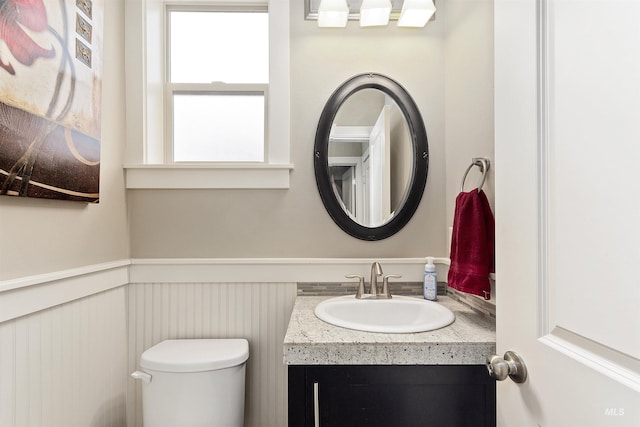 half bath featuring a wainscoted wall, toilet, and vanity