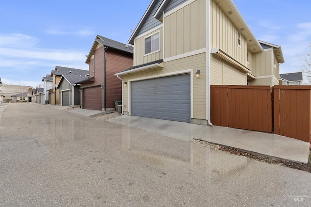 view of side of home featuring board and batten siding, an attached garage, and fence