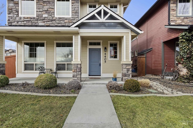 doorway to property featuring covered porch, stone siding, and a yard