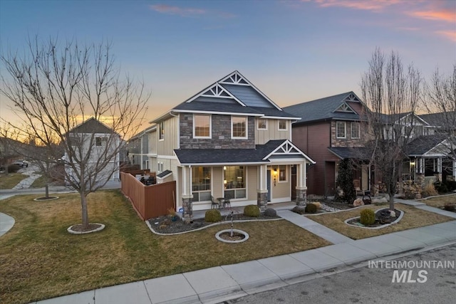 craftsman-style home featuring covered porch, fence, stone siding, a front lawn, and board and batten siding