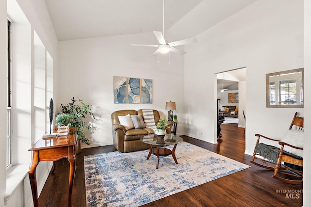 living room with a ceiling fan, high vaulted ceiling, baseboards, and wood finished floors