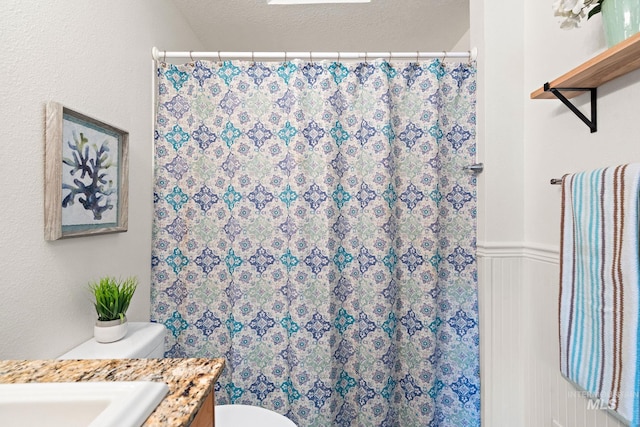 bathroom with toilet, a wainscoted wall, curtained shower, a textured ceiling, and vanity