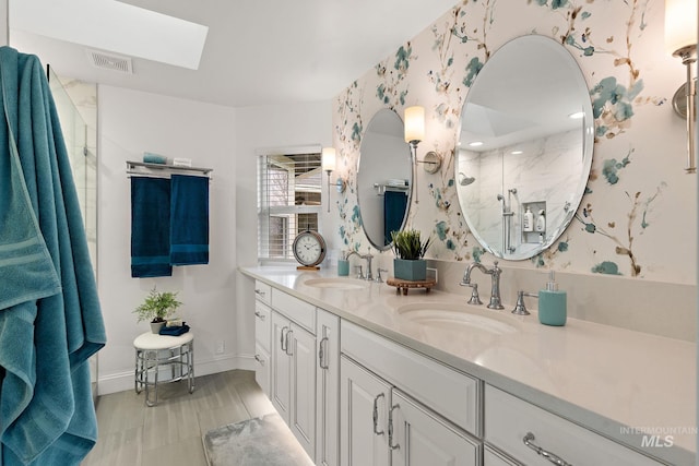 full bathroom featuring double vanity, a stall shower, a skylight, and a sink