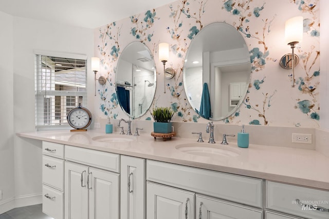 bathroom with double vanity, walk in shower, a sink, and wallpapered walls