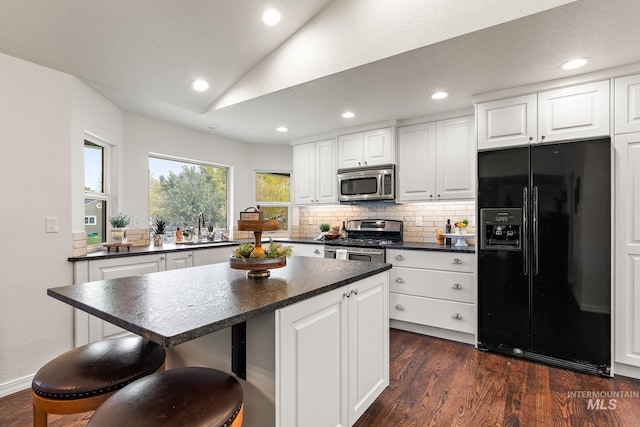 kitchen featuring dark countertops, dark wood-style floors, lofted ceiling, appliances with stainless steel finishes, and a sink