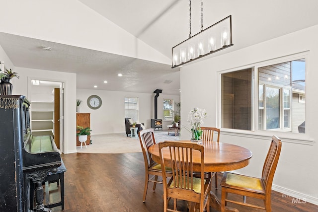 dining space with recessed lighting, wood finished floors, baseboards, vaulted ceiling, and a wood stove