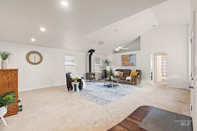 carpeted living area featuring visible vents, arched walkways, ceiling fan, a wood stove, and a textured ceiling