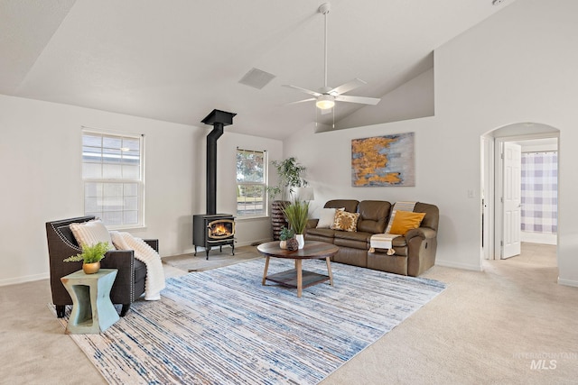 living room with arched walkways, ceiling fan, a wood stove, carpet, and high vaulted ceiling